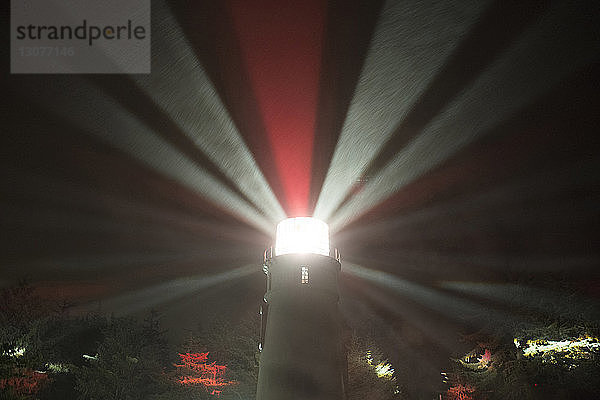 Niedrigwinkelansicht der vom Leuchtturm ausgehenden Lichtstrahlen gegen den Himmel bei Nacht