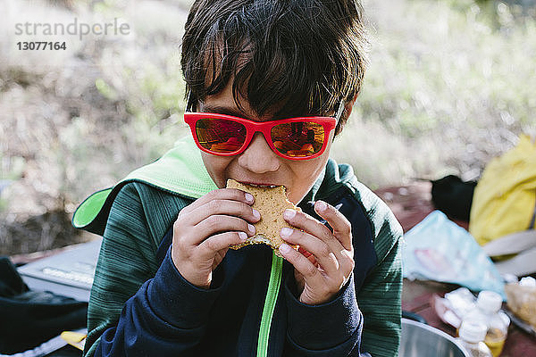 Junge mit Sonnenbrille isst Sandwich auf dem Campingplatz