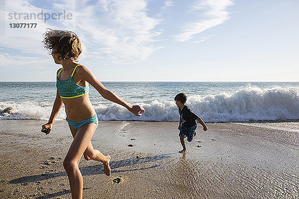 Mädchen und Junge rennen vor den rauschenden Wellen am Strand