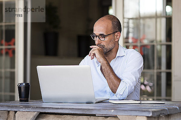 Geschäftsmann benutzt Laptop-Computer  während er im Büro am Tisch sitzt