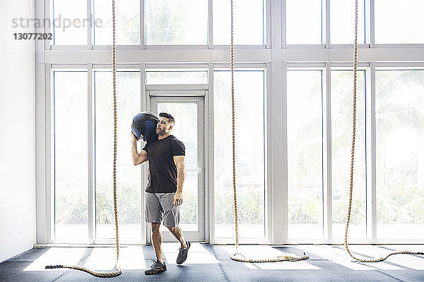 Männlicher Athlet  der einen Medizinball trägt  während er in einer Crossfit-Turnhalle trainiert