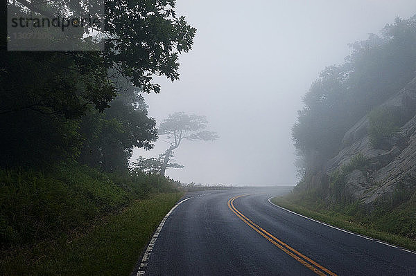 Leere Straße inmitten von Bergen gegen den Himmel bei nebligem Wetter
