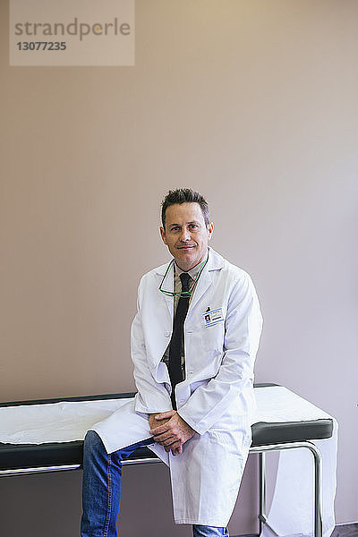 Porträt eines lächelnden Arztes  der auf dem Bett an der Wand sitzt