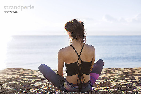 Rückansicht einer Frau  die am Strand am Ufer Yoga macht