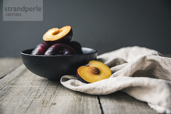 Nahaufnahme von Pflaumen in Schale mit Serviette auf Holztisch vor grauem Hintergrund