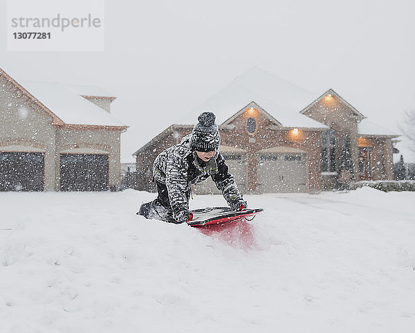 Junge rutscht bei Schneefall auf Schnee gegen Häuser