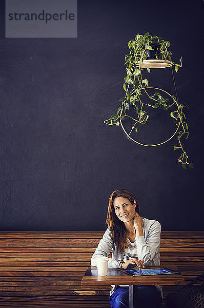 Porträt einer glücklichen Frau  die an einem Café-Tisch sitzt
