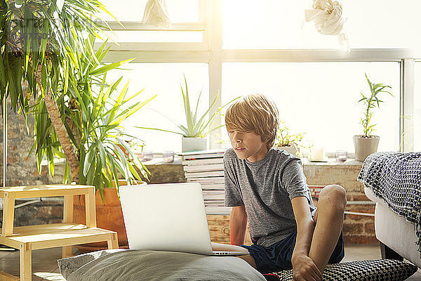 Junge schaut auf Laptop-Computer  während er auf dem Boden am Fenster sitzt