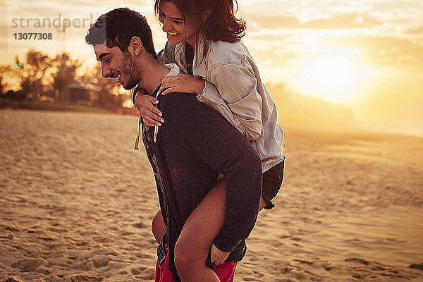 Mann nimmt seine Freundin am Strand Huckepack