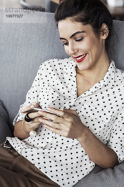 Glückliche Geschäftsfrau benutzt Smartphone  während sie im Restaurant auf dem Sofa sitzt
