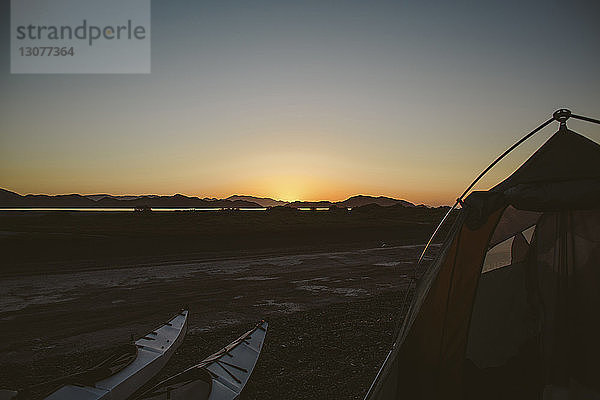 Kajaks an Land mit Zelt gegen klaren Himmel bei Sonnenuntergang