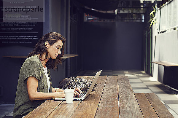 Seitenansicht einer Frau mit Laptop im Straßencafé
