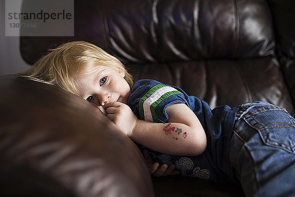 Süßer Junge schaut weg  während er sich zu Hause auf dem Sofa entspannt