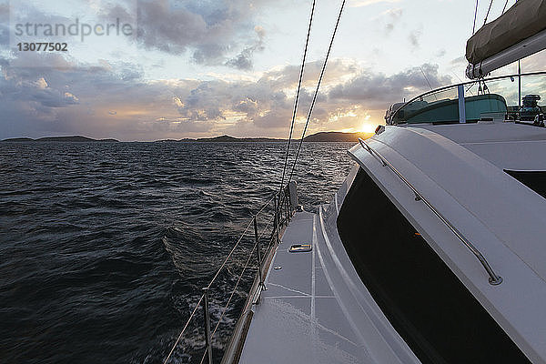 Segelboot fährt bei Sonnenuntergang auf See gegen bewölkten Himmel