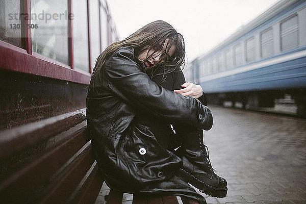 Porträt einer traurigen Frau  die während der Regenzeit auf einer Bank am Bahnhof sitzt