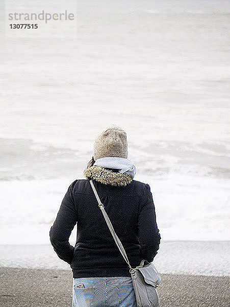 Rückansicht eines am Strand stehenden Teenagers in warmer Kleidung
