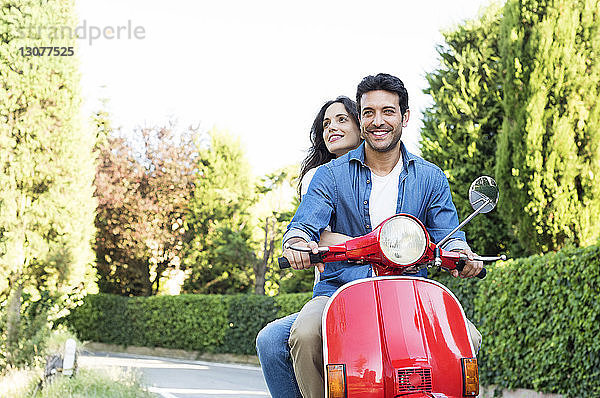 Lächelndes Paar auf einem Motorroller im Park