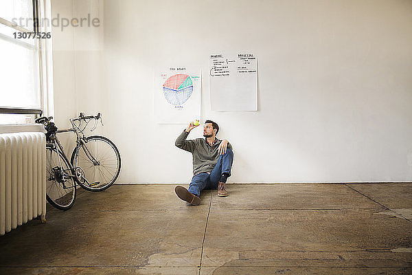 Geschäftsmann hält Ball  während er in einem kreativen Büro gegen Schaubilder an der Wand sitzt