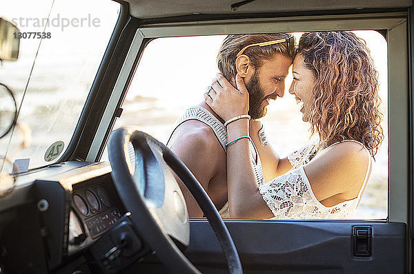 Fröhliches Paar schaut sich an  während es neben einem Geländewagen steht und durch ein Fenster gesehen wird