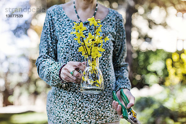 Mittelteil einer älteren Frau mit Blumenvase und Zange im Hof