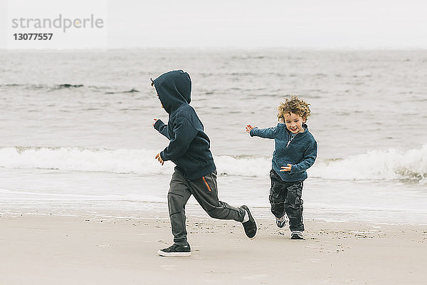 Glückliche Brüder spielen am Strand gegen den Himmel