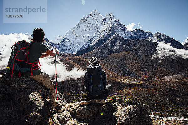 Freunde mit Rucksäcken sitzen auf Berg gegen blauen Himmel im Sagarmatha-Nationalpark