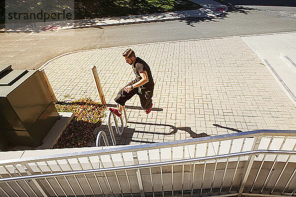 Hochwinkelaufnahme eines Mannes  der einen Stunt auf einem Geländer in der Stadt macht