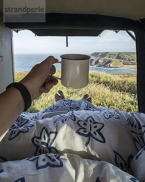 Niedriger Abschnitt eines Mannes  der eine Tasse hält  während er sich im Wohnmobil auf dem Bett entspannt