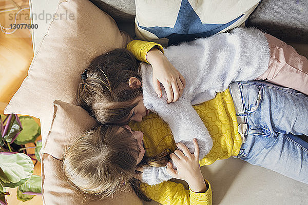Draufsicht auf Schwestern  die sich umarmen  während sie sich zu Hause auf dem Sofa entspannen