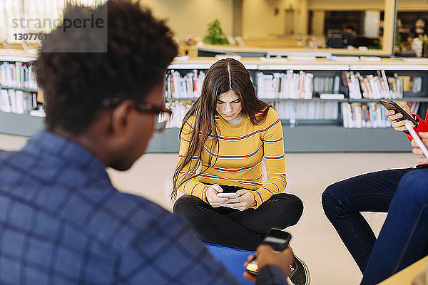 Freunde benutzen Smartphones  während sie in der Bibliothek sitzen