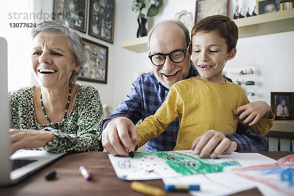 Fröhliche Großeltern mit Enkel beim Zeichnen zu Hause