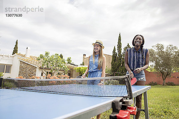 Glückliche Frauen spielen Tischtennis auf dem Hof