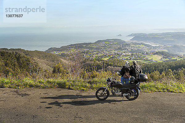 Älteres Ehepaar mit Blick auf die Berge  während es mit dem Motorrad auf der Straße steht
