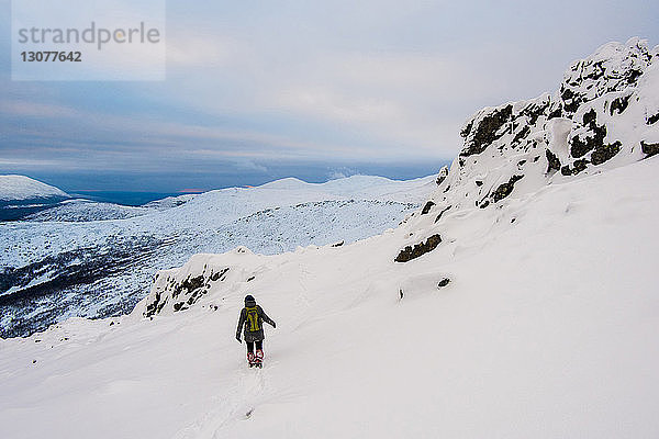 Wanderer auf schneebedecktem Berg vor bewölktem Himmel