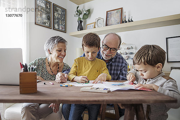 Glückliche Großeltern sehen zu Hause Enkel beim Zeichnen