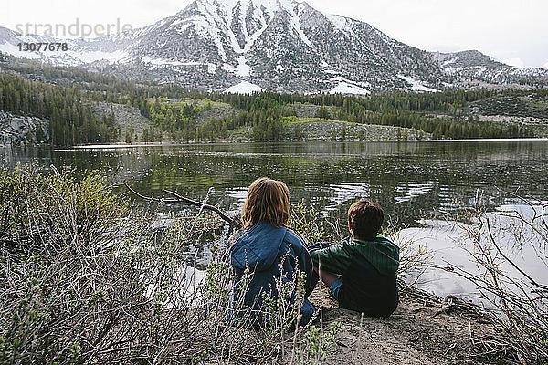 Rückansicht von Geschwistern  die am See im Inyo National Forest sitzen