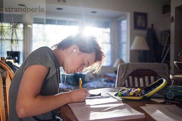Seitenansicht einer Teenagerin  die Musik hört  während sie zu Hause Hausaufgaben schreibt