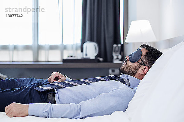 Seitenansicht eines Geschäftsmannes mit Augenmaske beim Schlafen im Hotelzimmer