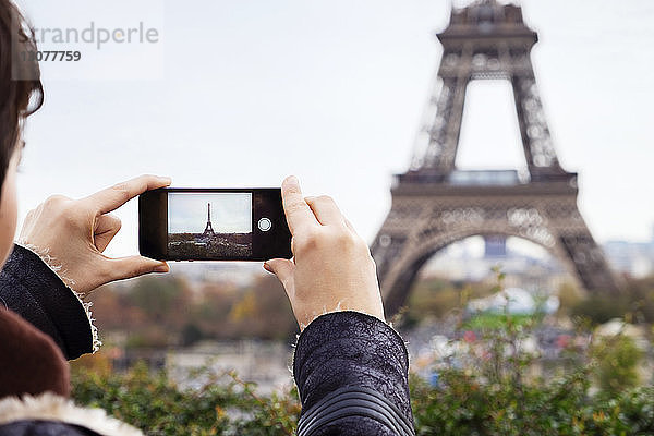 Junge Frau fotografiert Eiffelturm mit Smartphone