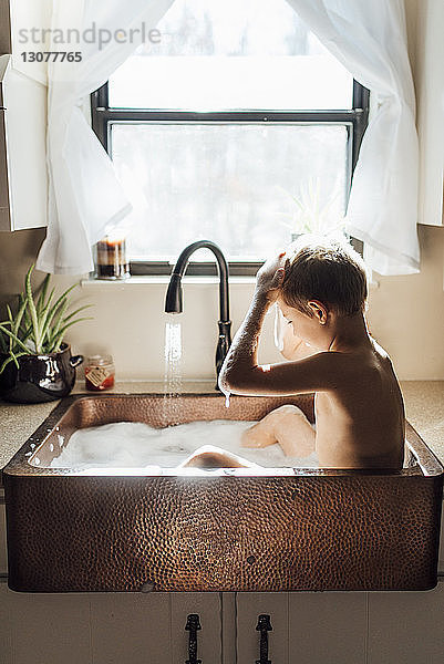 Junge ohne Hemd badet  während er zu Hause in der Küchenspüle sitzt