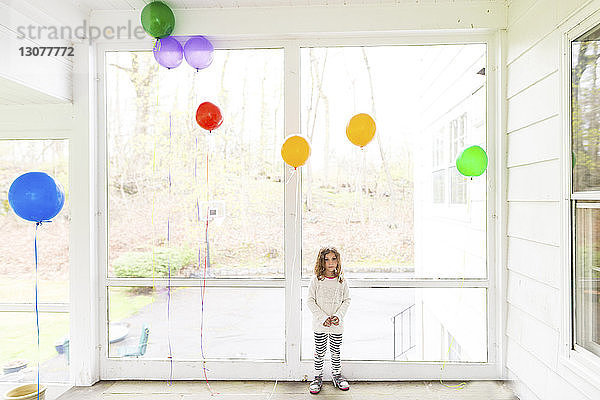 Mädchen in voller Länge mit Luftballons zu Hause stehend