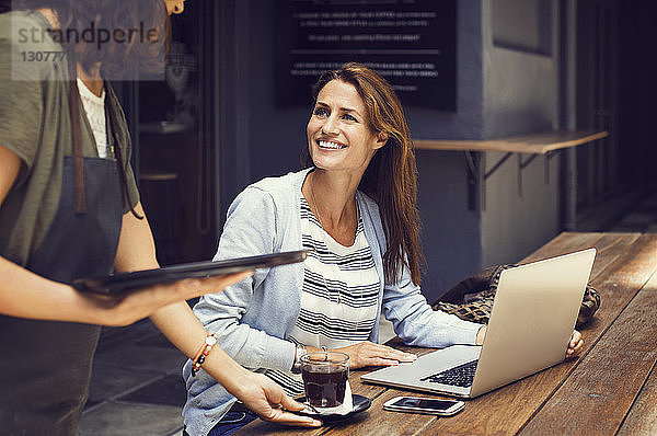 Glückliche Frau sieht Kellnerin an  die im Straßencafé Kaffee serviert