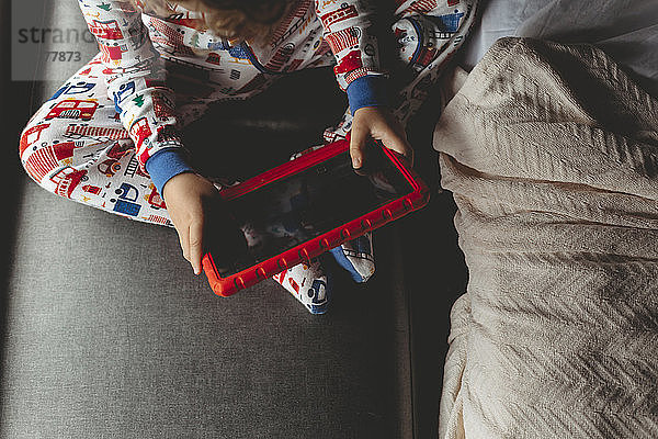 Hochwinkelansicht eines Jungen  der einen Tablet-Computer benutzt  während er zu Hause auf dem Sofa sitzt