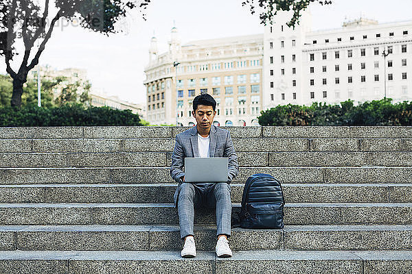 Geschäftsmann mit Laptop-Computer  während er mit einer Tasche auf der Treppe sitzt