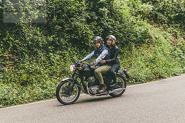 Paar fährt Motorrad auf der Straße zwischen Bäumen im Wald