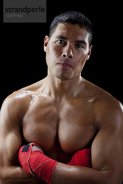 Porträt eines selbstbewussten Boxers ohne Hemd mit verschränkten Armen vor schwarzem Hintergrund