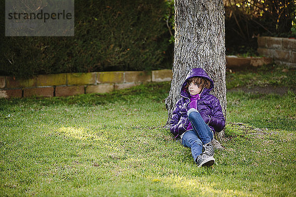 Nachdenkliches Mädchen entspannt sich auf Grasfeld bei einem Baum im Park