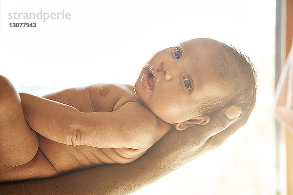 Ausgeschnittenes Bild eines Vaters  der ein süßes Baby aus einem hell erleuchteten Fenster trägt