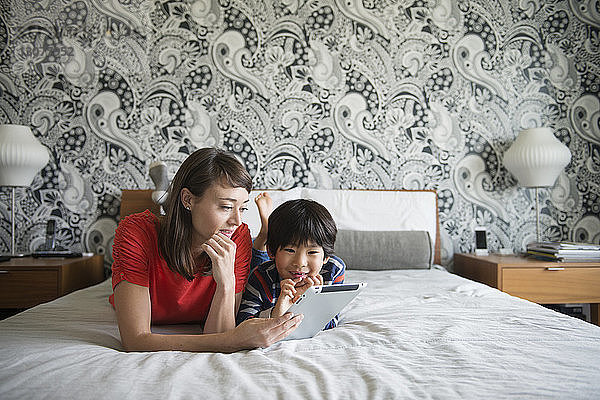 Mutter und Sohn benutzen ein digitales Tablett  während sie auf dem Bett liegen