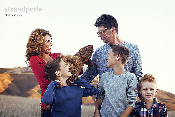 Glückliche Familie mit Hund auf dem Feld vor klarem Himmel stehend